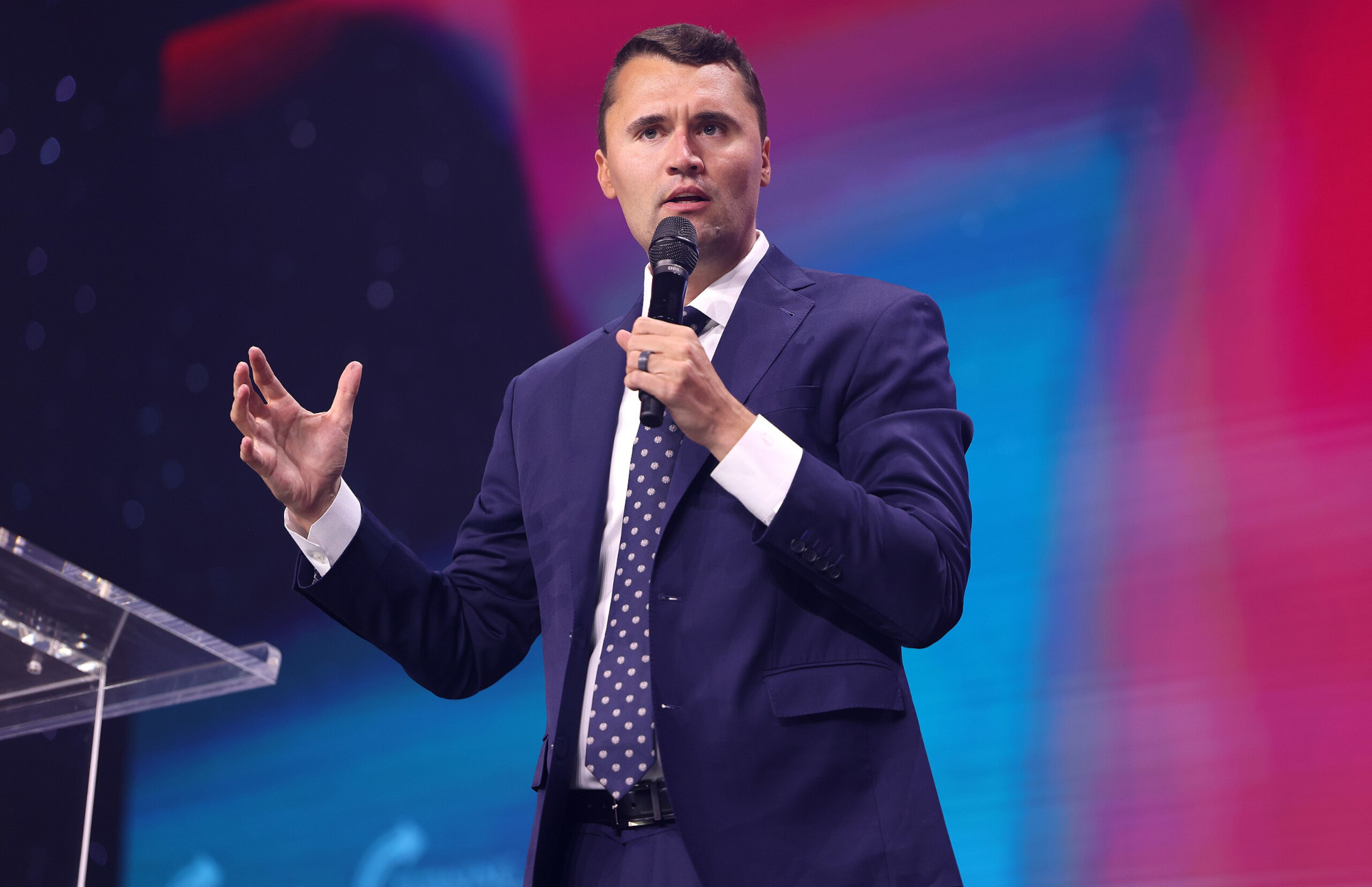 Charlie Kirk with a microphone, speaking onstage at a conference