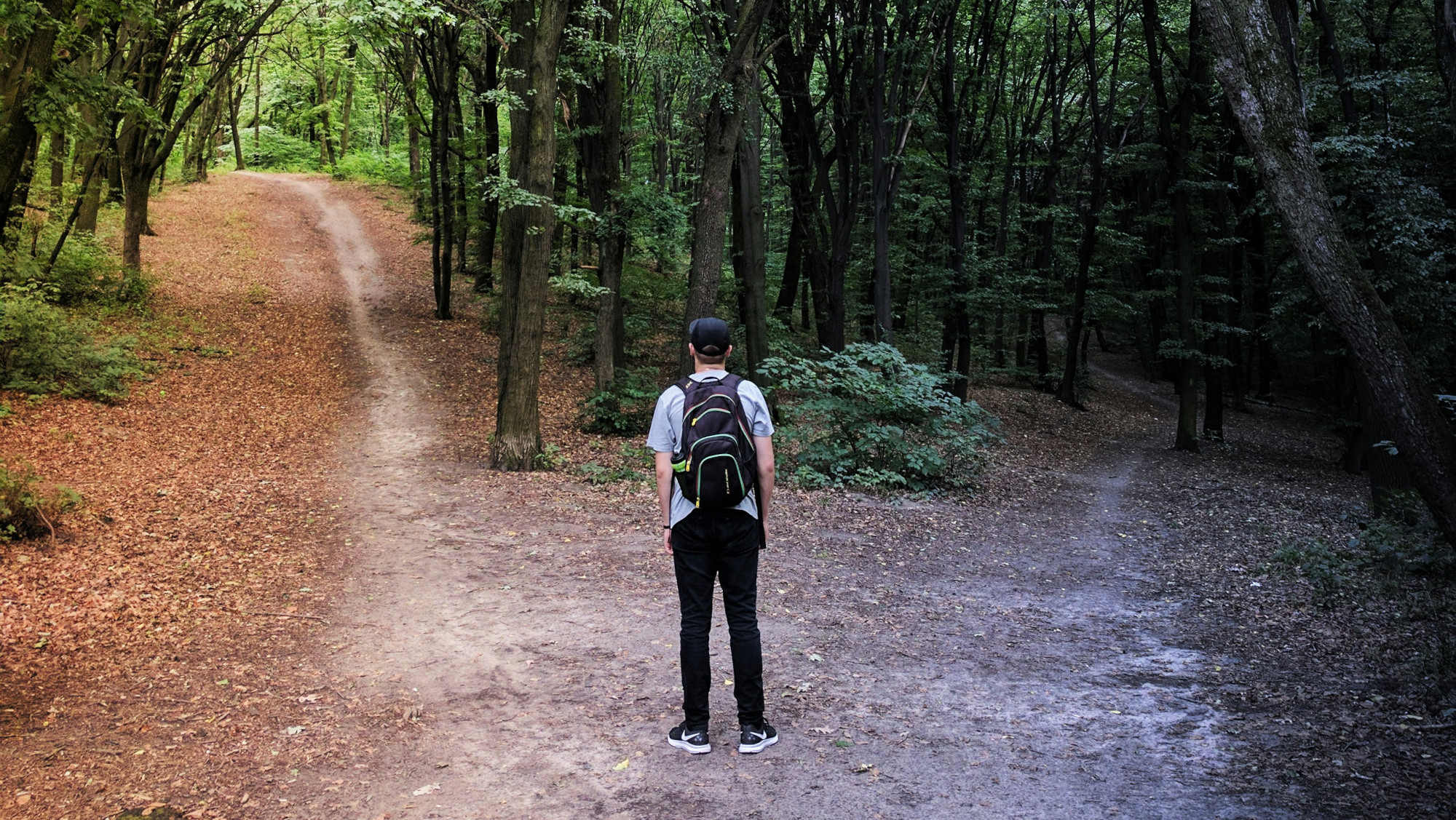 Backpacker in the woods staring at a fork in his path
